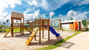 Un parque infantil con una estructura de madera para escalar, toboganes y una zona vallada.