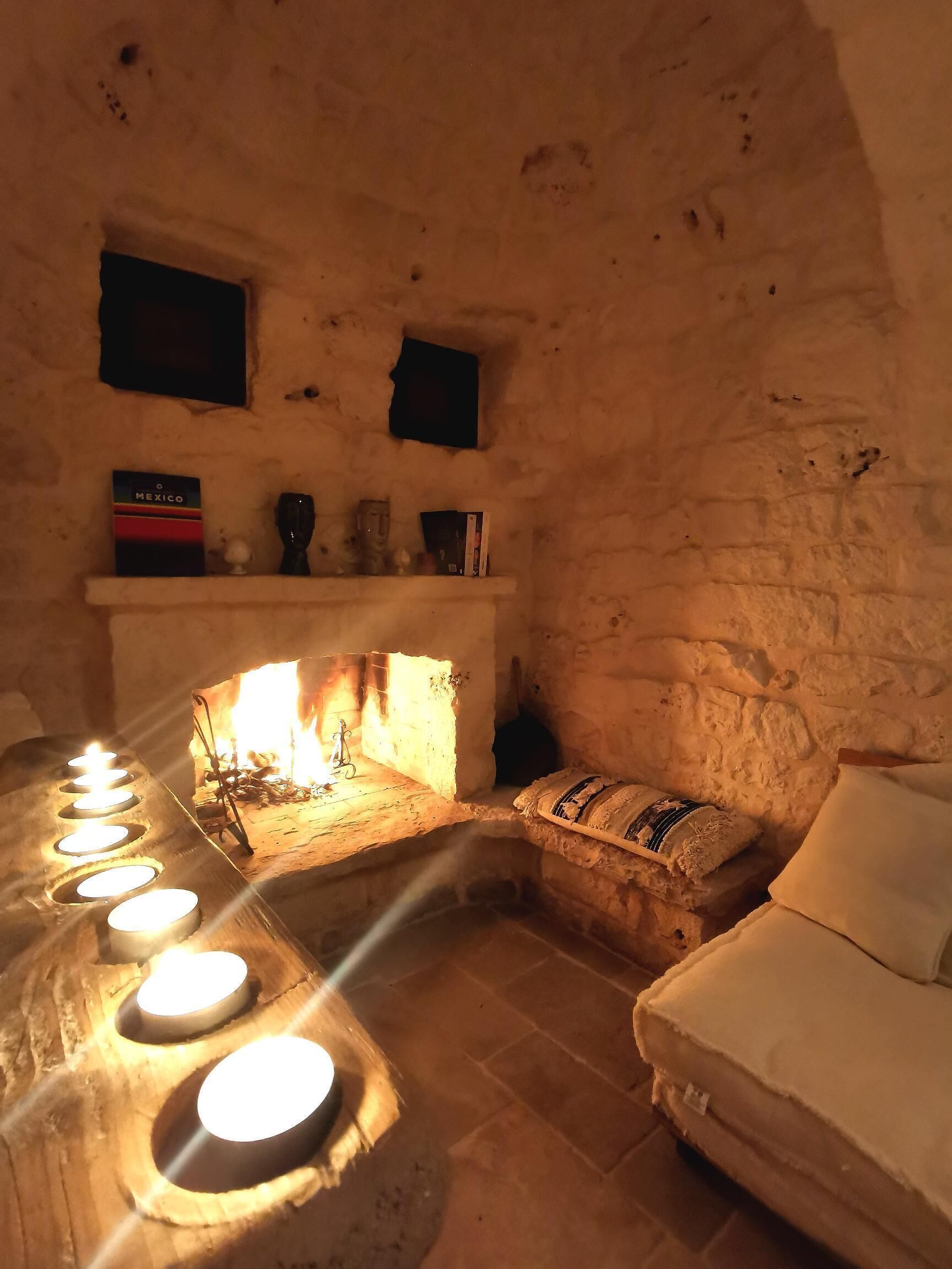 A cozy room with a stone fireplace, a white sofa, and a shelf with books and decorative items.