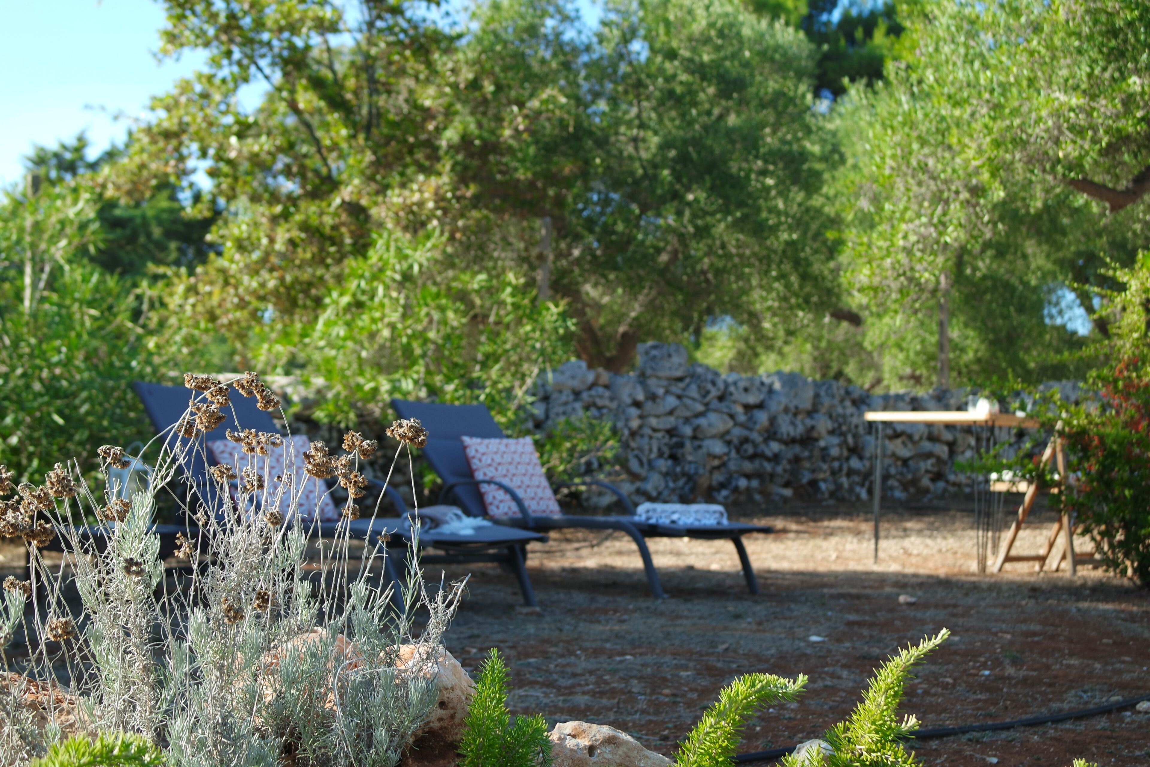 A garden with a stone wall, a lounge chair, and a table.
