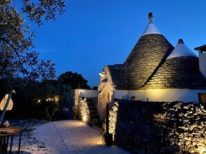 A stone building with a conical roof, surrounded by a garden with cacti and a pathway leading to the entrance. - A romantic trullo with a private pool surrounded by nature (Ceglie Messapica)