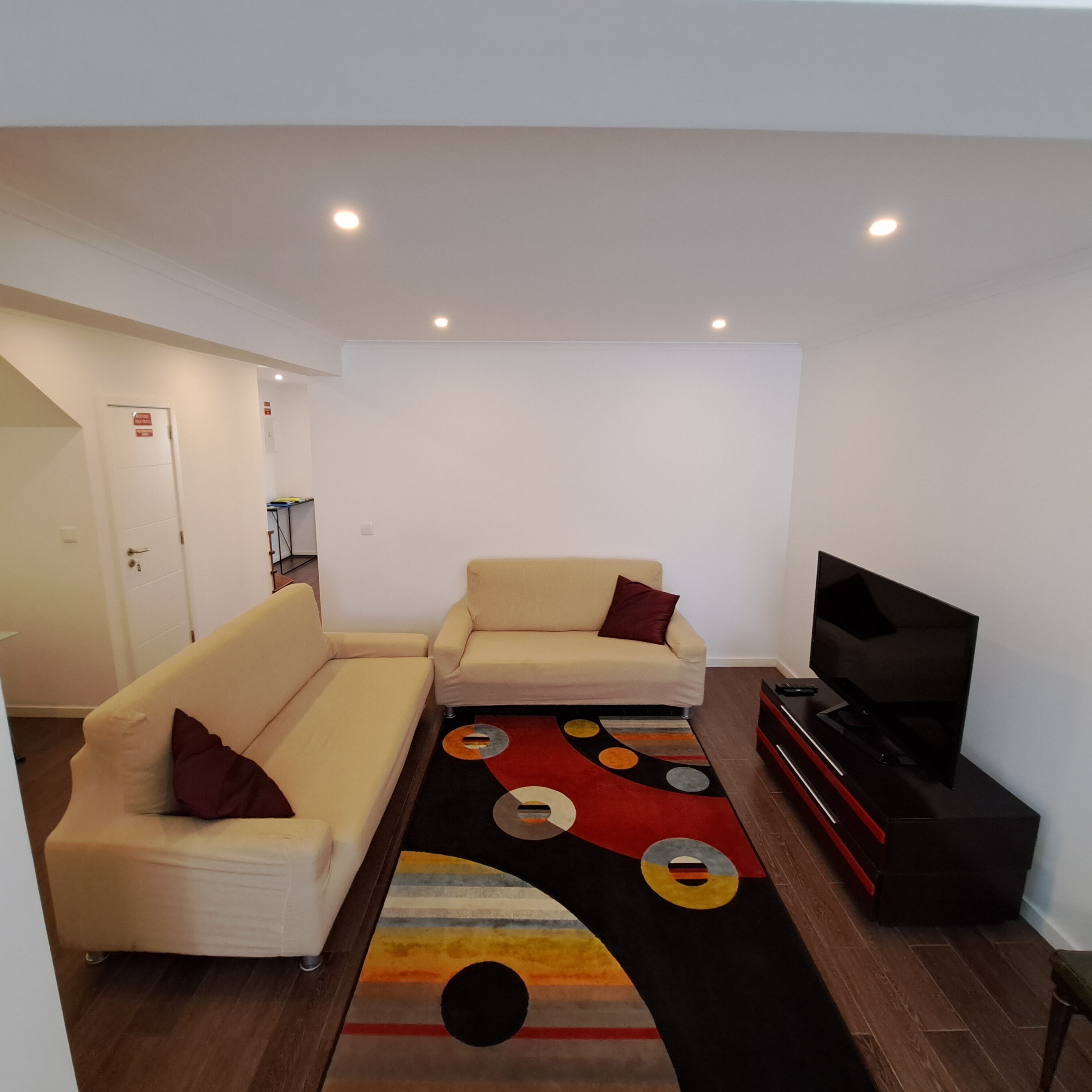 Ein Wohnzimmer mit einer Couch, einem TV-Schrank und einem gemusterten Teppich.
