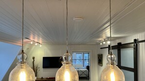 Una sala de estar moderna con un sofá blanco, un televisor grande y tres lámparas colgantes.