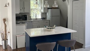 Una cocina moderna con una isla central, taburetes de bar, lámparas colgantes y vistas al exterior a través de un ventanal.