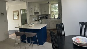 Una cocina moderna con armarios blancos, una isla azul, electrodomésticos de acero inoxidable e iluminación colgante.