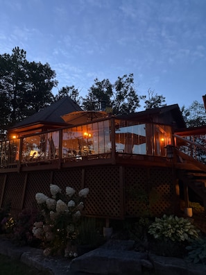 A wooden deck with glass railings overlooking a garden with white flowers.