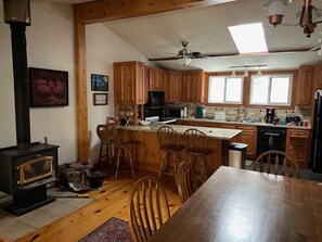 Een keuken met houten kasten, een fornuis en een eethoek met stoelen.