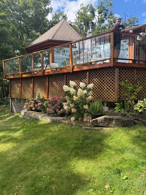 A wooden deck with glass railings, surrounded by a garden with hydrangeas and other plants.
