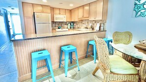 Une cuisine moderne avec des meubles en bois, un îlot central doté de tabourets, un four à micro-ondes et un réfrigérateur.