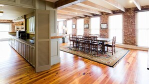 Une cuisine spacieuse avec des meubles en bois et un grand îlot central, un coin repas avec une table et des chaises en bois, et des murs en briques agrémentés de grandes fenêtres.
