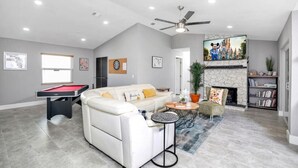 A spacious living room with a pool table, a white sofa, a fireplace, and a ceiling fan.