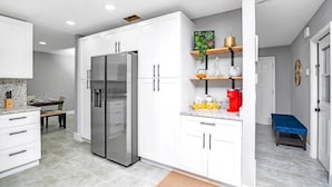 A modern kitchen with white cabinets, a stainless steel refrigerator, and a dining area with a bench.