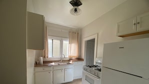 A kitchen with white cabinets, a gas stove, a refrigerator, and a window with curtains.