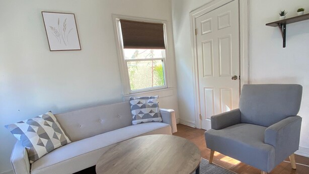 A living room with a sofa, armchair, round coffee table, and a window with blinds.