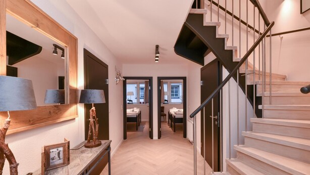 A modern interior with a wooden staircase, a hallway leading to a bedroom, and a desk with a lamp. - Penthouse Lake Mountains View Incl Summer Card (Zell am See)