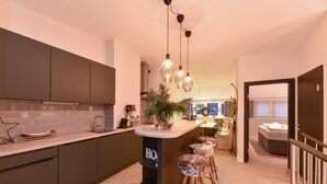 A modern kitchen with dark cabinets, a central island, and hanging pendant lights. - Penthouse Lake Mountains View Incl Summer Card (Zell am See)