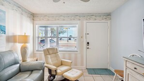 Ein Zimmer mit einer Couch, einem Liegestuhl, einem Schreibtisch und einem Fenster mit Jalousien.