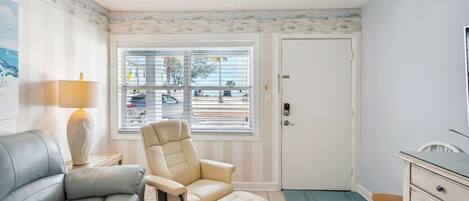 A room with a sofa, a recliner, a desk, and a window with blinds.