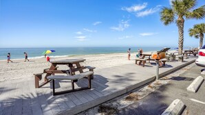 Ein Strand mit Picknicktischen und Bänken, Palmen und blauem Himmel.