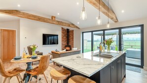 A modern kitchen with a large island, wooden beams, and a fireplace. - The Workshop - UK42470 (Pickering)