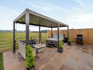 A covered patio area with a hot tub, outdoor seating, and a grill.