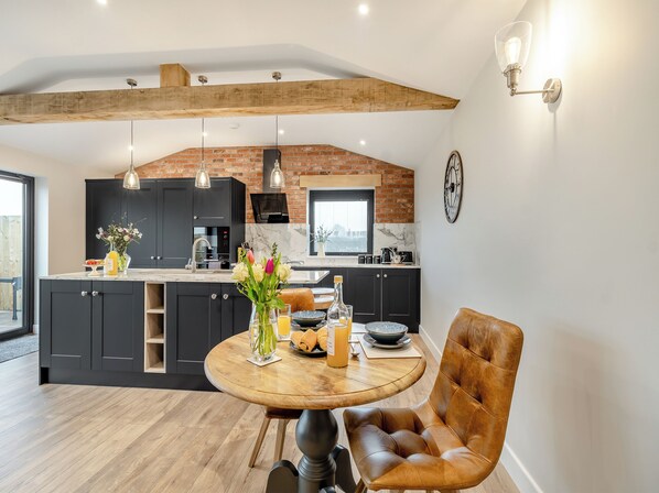 A modern kitchen with dark cabinets, a wooden dining table, and a leather chair.