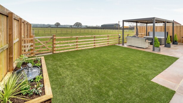 A backyard with a wooden fence, a grassy lawn, a pergola with seating, and a small water feature. - The Workshop - UK42470 (Pickering)