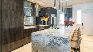 Una cocina moderna con una isla de mármol, muebles oscuros, electrodomésticos de acero inoxidable y una amplia zona de bar con asientos.