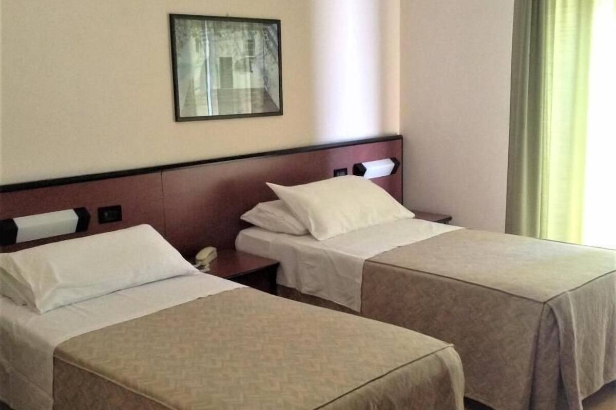 Une chambre d’hôtel avec deux lits simples, une table de chevet avec un téléphone et un tableau encadré au mur.