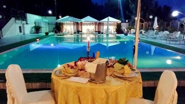 Ein Esstisch für zwei Personen mit Blick auf einen Pool, Außenbereich mit Sitzgelegenheiten und Sonnenschirmen im Hintergrund.