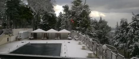 A snow-covered outdoor area with a pool, umbrellas, and a railing.
