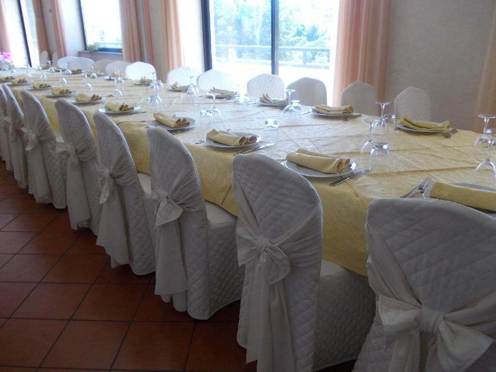 Un salón de banquetes con largas mesas dispuestas para un evento formal, cada una con manteles blancos y fundas para sillas a juego.