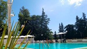 Ein Swimmingpool mit Liegestühlen und Sonnenschirmen, umgeben von Bäumen.