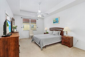 Une chambre à coucher comprenant un lit, des tables de chevet, un bureau, une chaise, un ventilateur de plafond et une fenêtre.