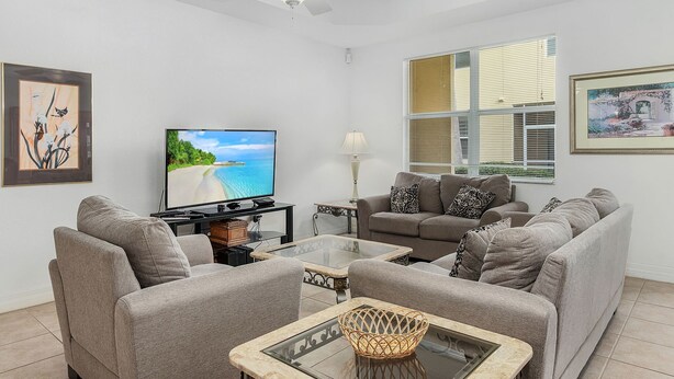 Een woonkamer met een flatscreen televisie, grijze banken, een glazen salontafel en een plafondventilator.