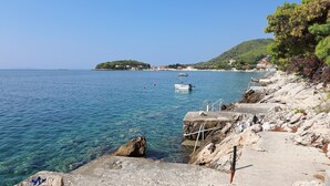 A coastal scene with clear blue water, a rocky shoreline, and a small island with buildings in the distance. - Seaside Apartments Markota - Two Bedroom Apartment with Terrace and Sea View (Prižba)