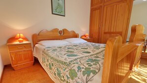 Ein Schlafzimmer mit einem hölzernen Bett, Nachttischen mit Lampen, einem Holzschrank und einer blumigen Tagesdecke.