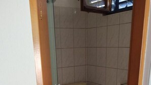 Et lille badeværelse med fliser, toilet, håndvask og bruseområde.