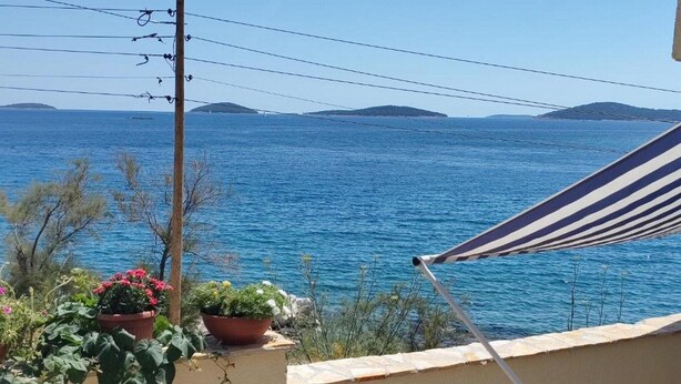En balkon med havudsigt, plantekasser og en stribet strandparasol.