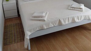 Una cama bien hecha con sábanas blancas y dos toallas dobladas, una lámpara de noche y un cuadro de un paisaje en la pared.