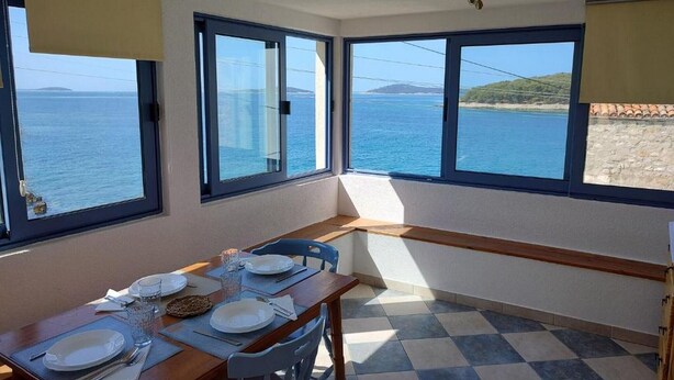 Un comedor con una mesa dispuesta para dos, ventanas amplias con vista al mar y un suelo de cuadros.