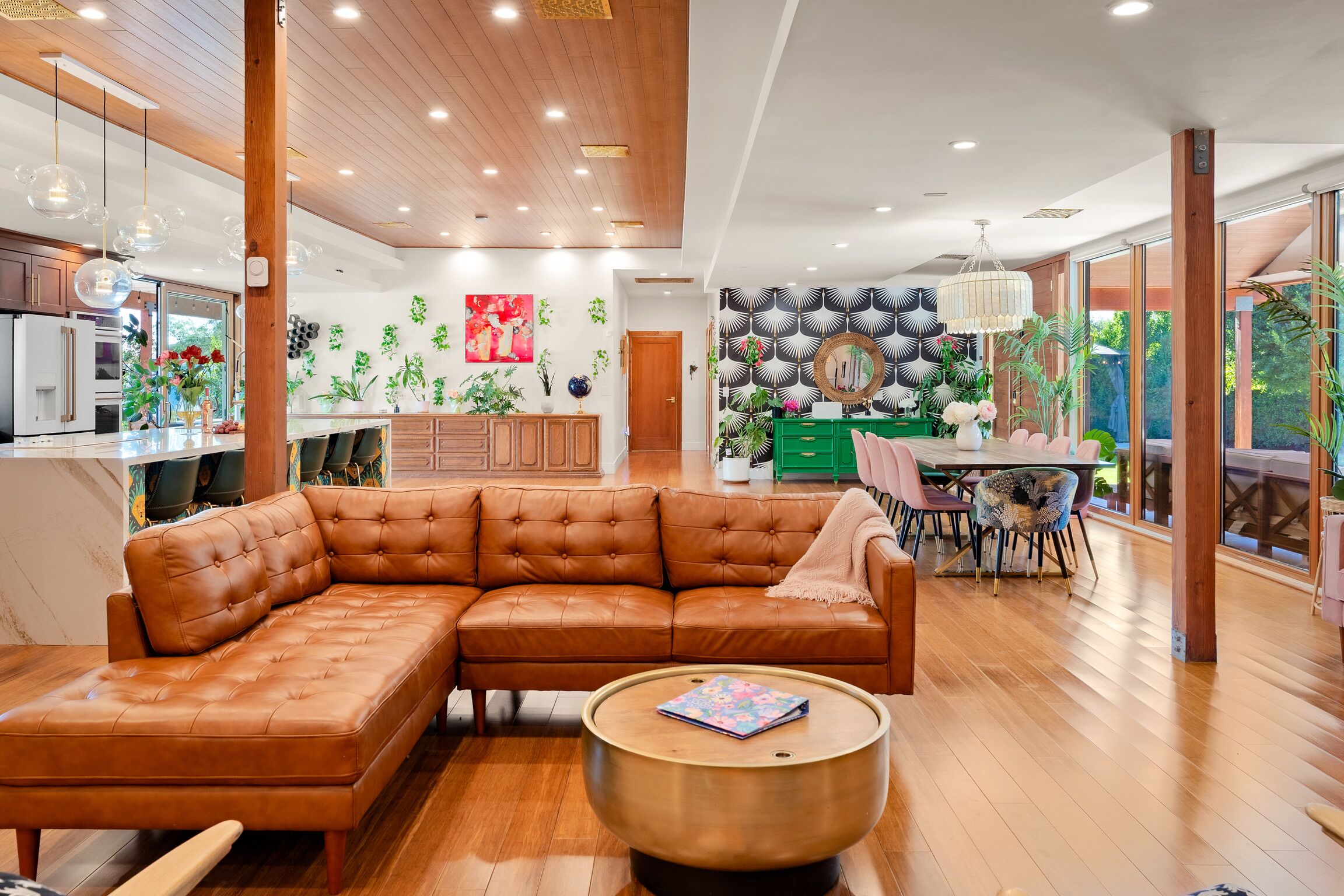 A spacious living area with a large brown leather sectional sofa, a round wooden coffee table, and a dining area with a green table and chairs.