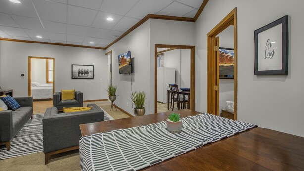 Een moderne woonkamer met een bank, een eettafel en een keuken, zichtbaar door een open deur.