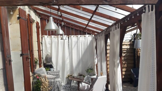 Un patio couvert avec un sol en bois, une table entourée de chaises, des plantes en pot et une statue.