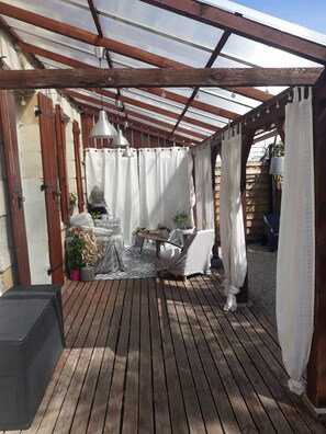 Un patio couvert avec un sol en bois, une table entourée de chaises, des plantes en pot et une statue.