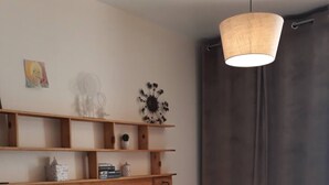 Une chambre à coucher avec une tête de lit en bois, un lit recouvert d’une literie à motifs, un luminaire suspendu et une étagère ornée d’objets décoratifs.