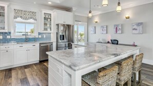 Una cocina moderna con armarios blancos, una isla grande y un comedor con sillas de mimbre.