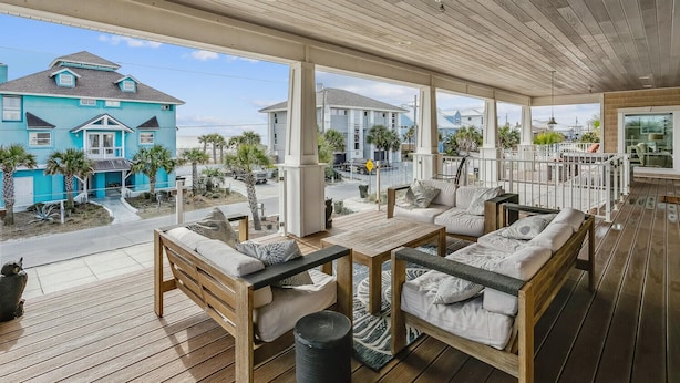 Un espacio de estar techado al aire libre con mobiliario de madera y vista a un edificio turquesa.