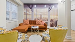 A living room with a sectional sofa, two armchairs, a small round table, and a large window with a cityscape view.