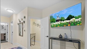 A bedroom with a bed, a TV mounted on the wall, a console table, and a door leading to another room.