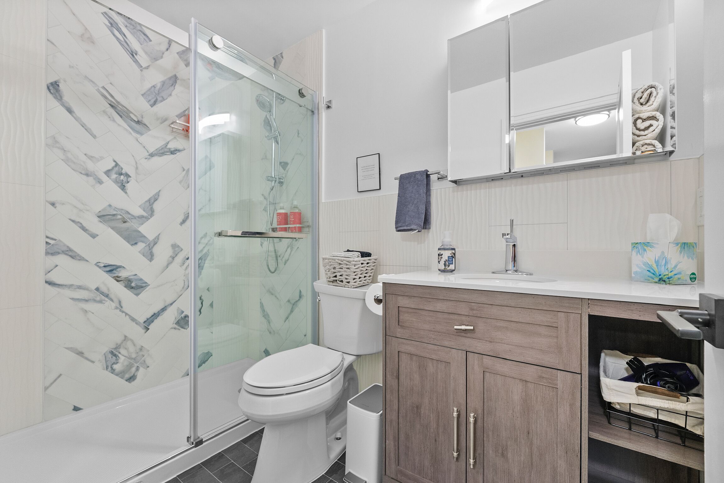 A modern bathroom with a glass shower enclosure, a toilet, a vanity with a sink, and a mirror.